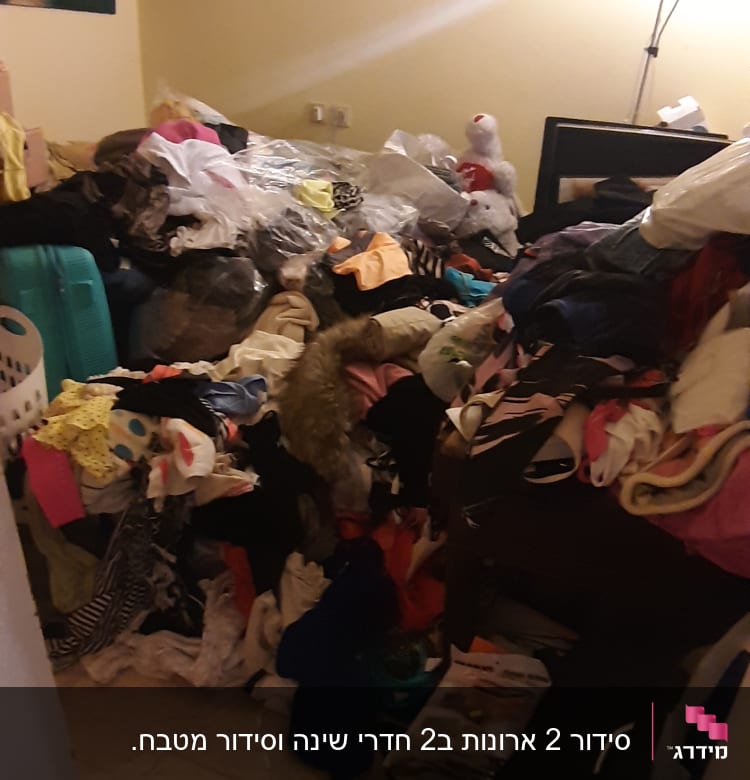 חדר עם ערימות בגדים וצעצועים מפוזרים על הרצפה